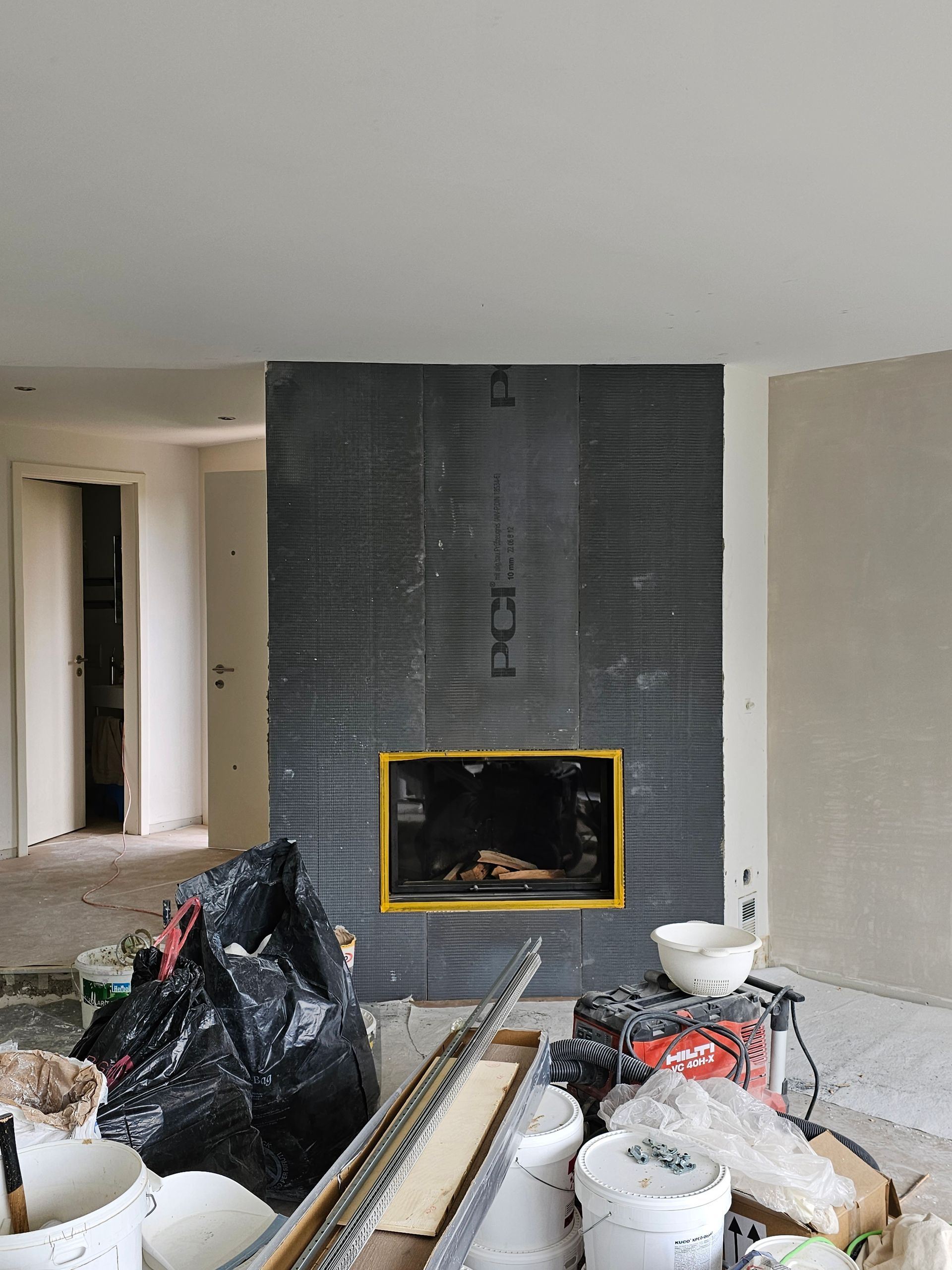 Eine Person in Overall und Schutzhelm streicht mit einer Farbrolle eine weisse Wand.