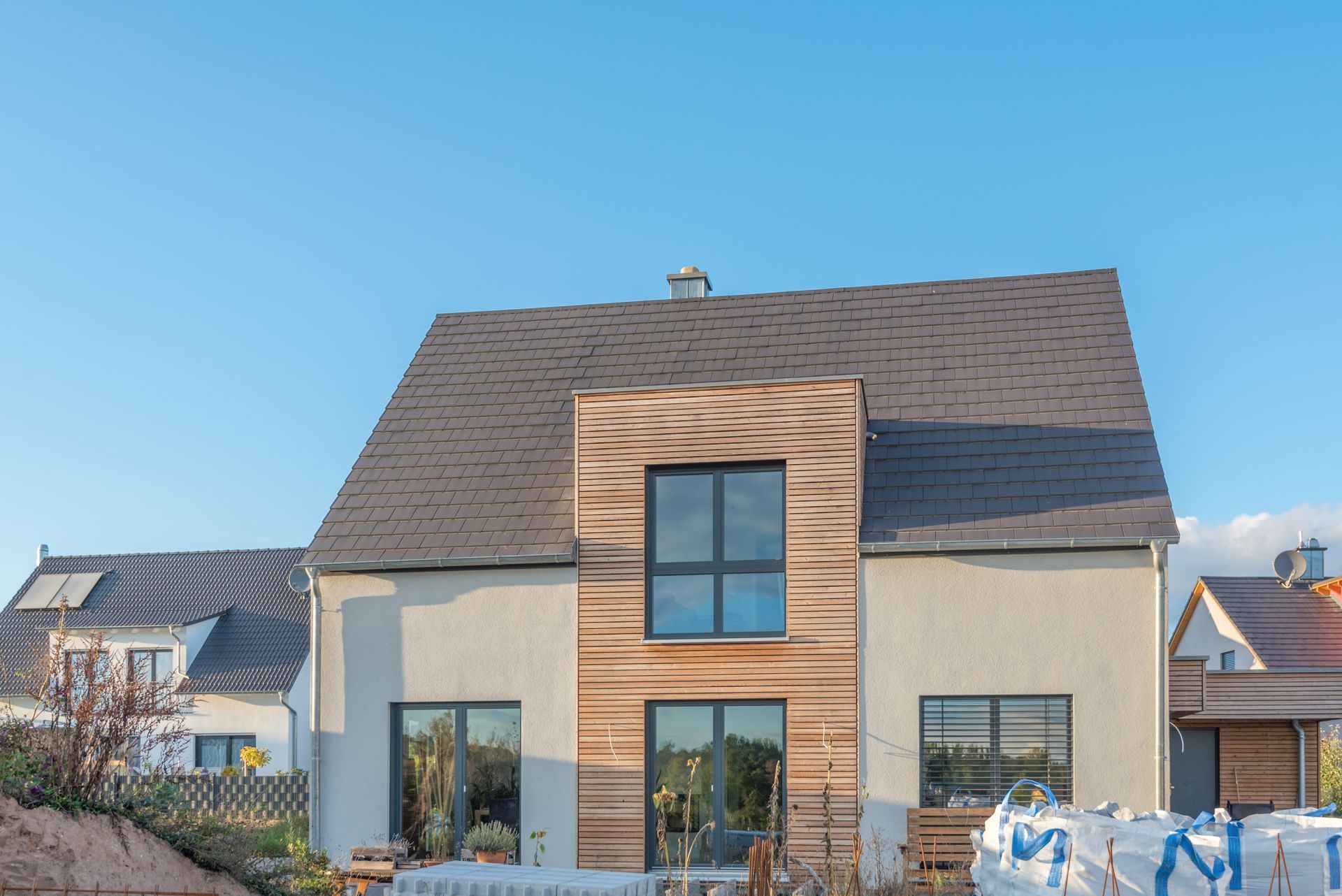 Eine Person in Overall und Schutzhelm streicht mit einer Farbrolle eine weisse Wand. 