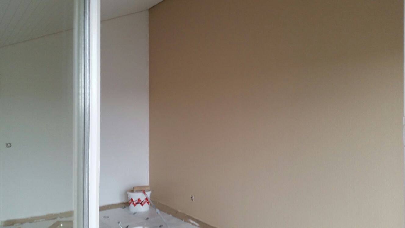 Das Zimmer ist innen mit beigen und weissen Wänden, weissen Zierleisten und einem Farbeimer auf dem Boden ausgestattet.