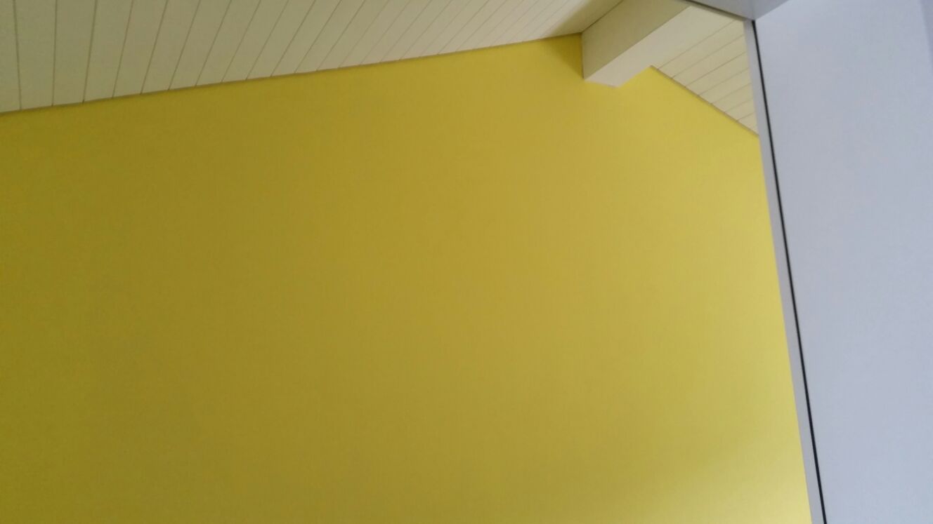 Eine gelb gestrichene Wand trifft auf eine weisse Decke und eine Türrahmenecke.