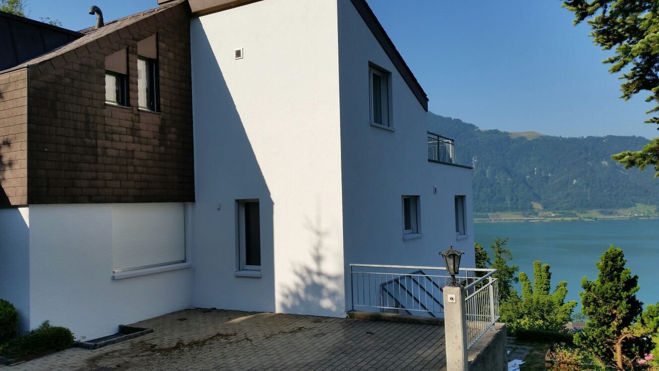 Maler in blauem Overall und mit Kappe auf einer Leiter, der mit einer Farbrolle eine hellblaue Wand streicht.