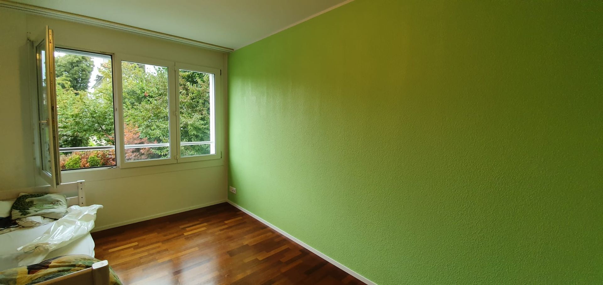 Zwei Maler in weissen Overalls streichen eine weisse Wand in einem Zimmer, einer von ihnen auf einer Leiter, mit Farbrollen.