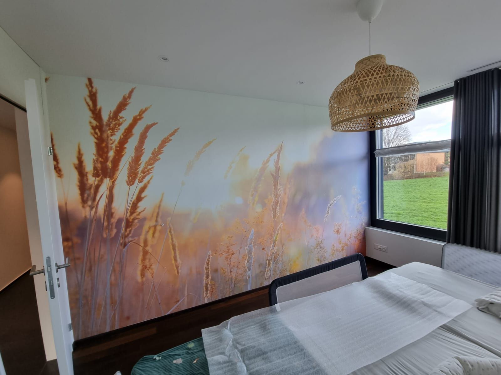 Eine Person in Overall und Schutzhelm streicht mit einer Farbrolle eine weisse Wand. 