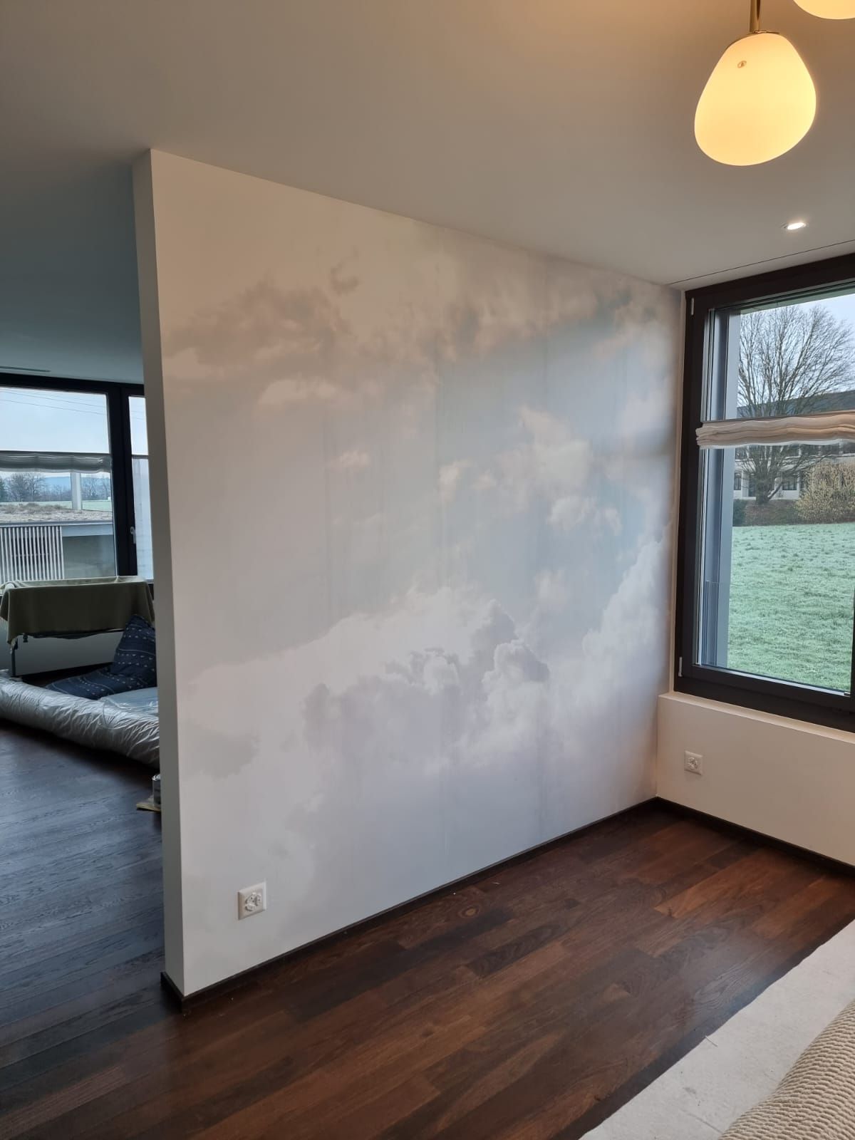 Zwei Personen streichen eine Wand in einem Zimmer; eine auf einer Leiter, die andere auf dem Boden, mit Farbrollen.