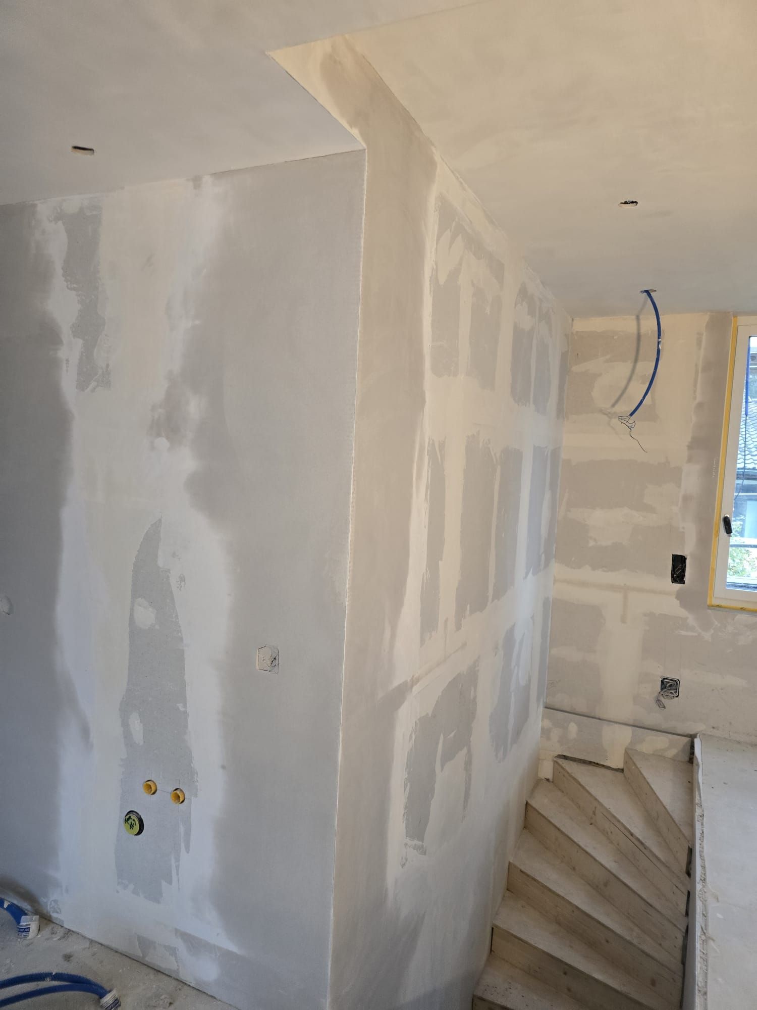 Zwei Maler in weissen Overalls streichen eine weisse Wand in einem Zimmer, einer von ihnen auf einer Leiter, mit Farbrollen.