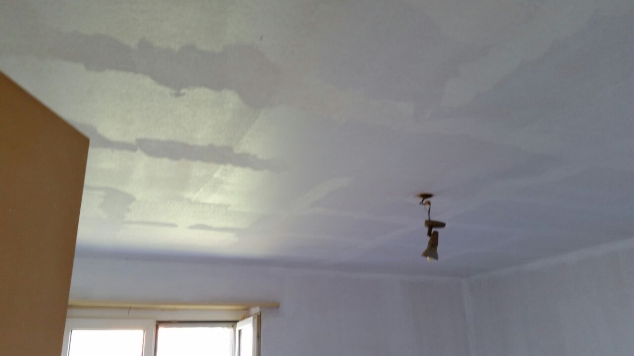 Weisse Decke mit Wasserflecken, eine Lampe und ein Fenster.