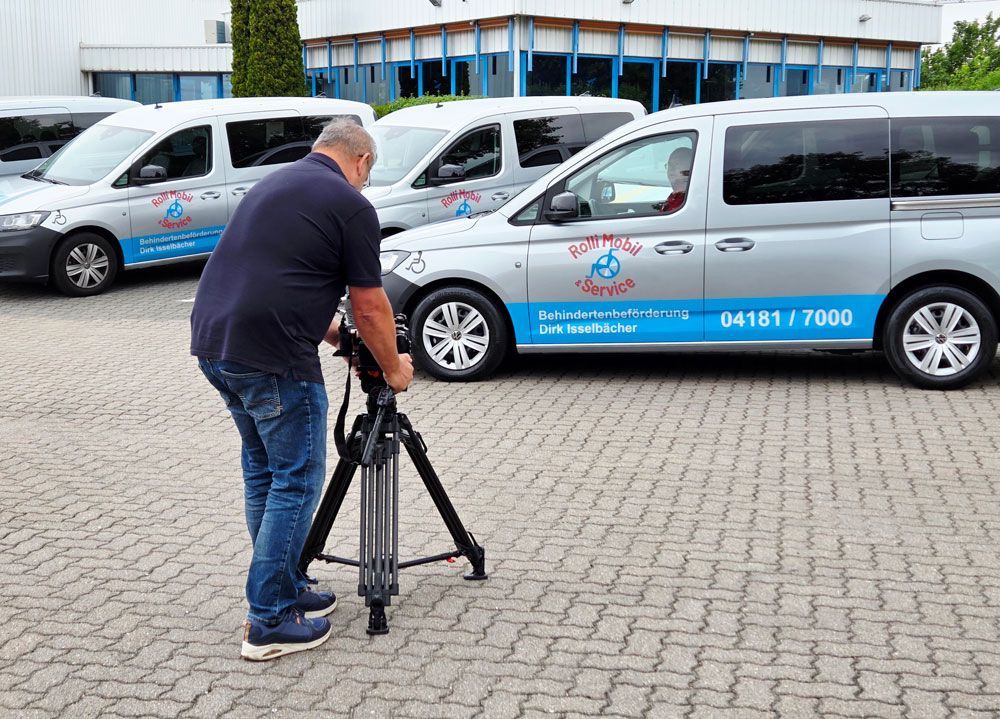 Man adjusting a tripod beside white-and-blue vans in a parking lot