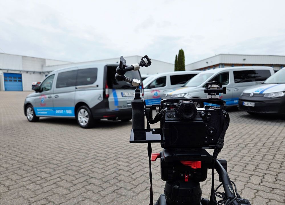 Camera filming a row of silver vans in a parking lot, with a tripod in the foreground