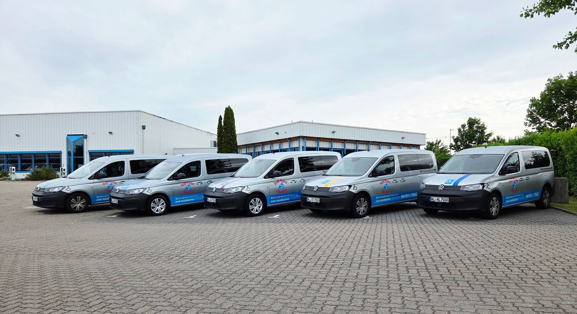 Row of white and blue utility vans parked in front of a warehouse on a paved lot