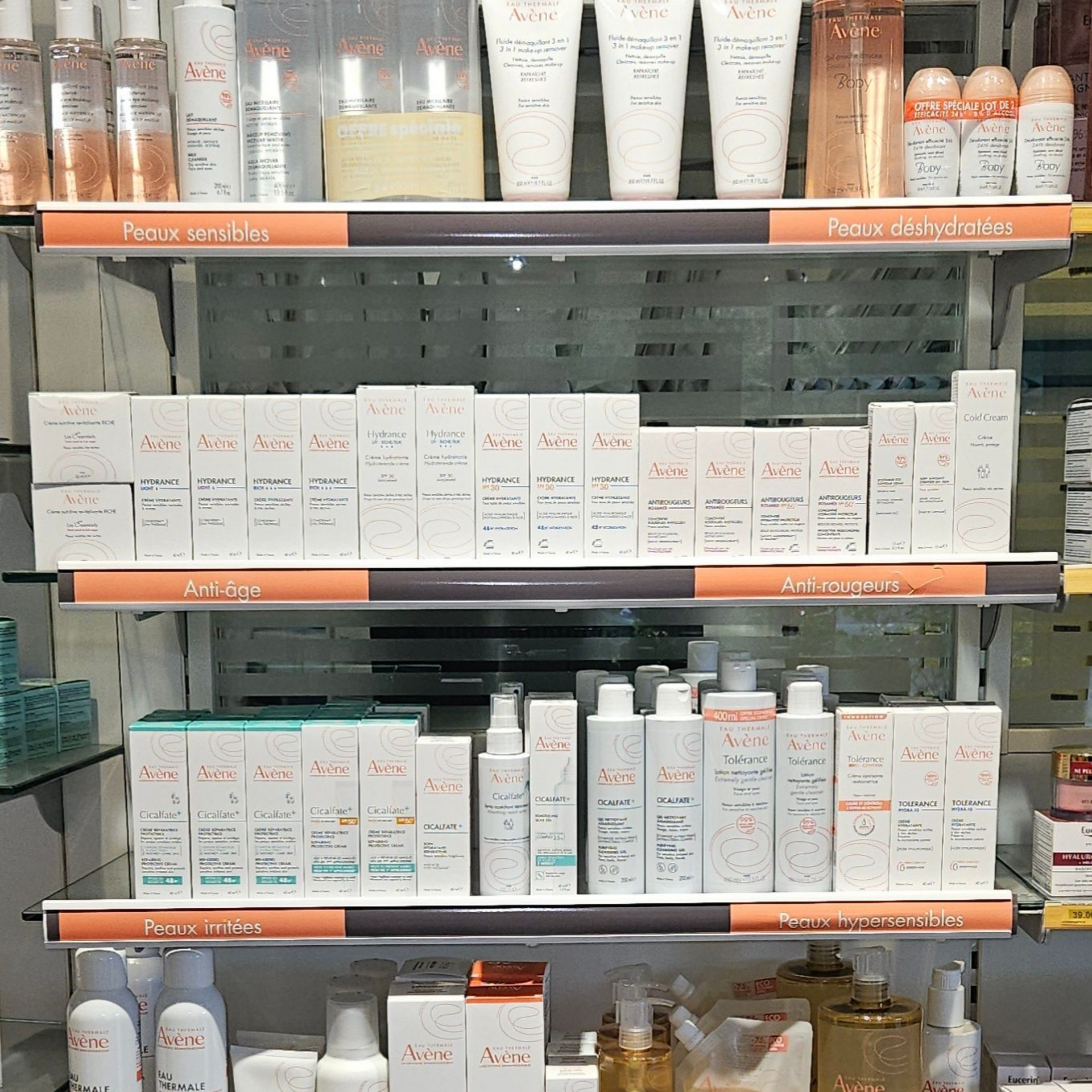 Rayon du magasin garni de produits de soins de la peau en boîtes et en flacons, dans des emballages blancs, oranges et bleus.