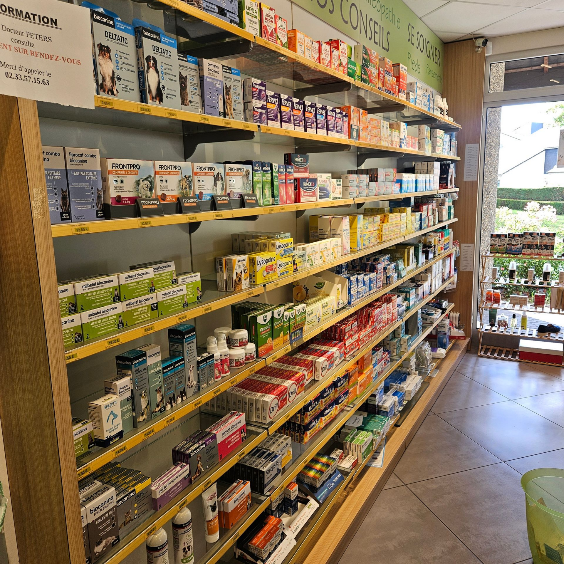 Des étagères remplies de produits emballés dans une petite allée de magasin, avec une entrée lumineuse au fond.