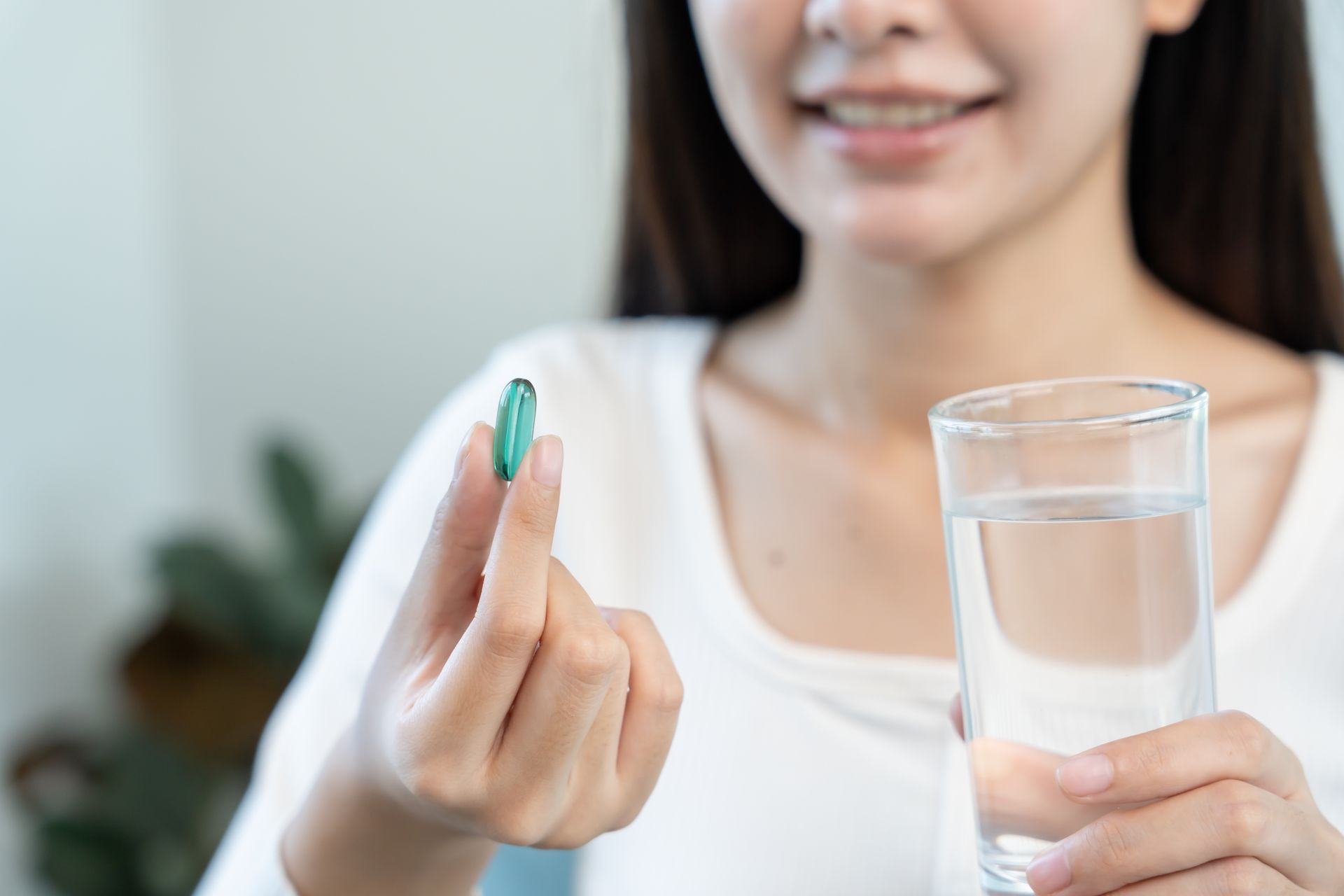 Une femme tenant une pilule verte et un verre d'eau à l'intérieur