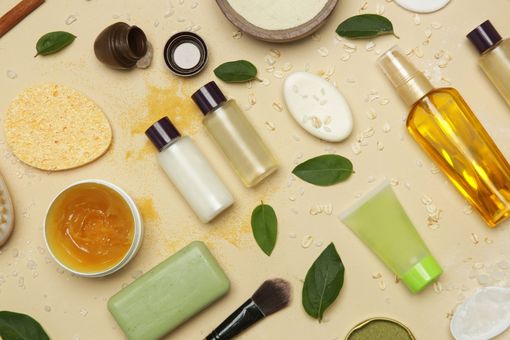 Produits de soin variés et feuilles disposés sur un fond beige, avec un pinceau et une éponge à maquillage.