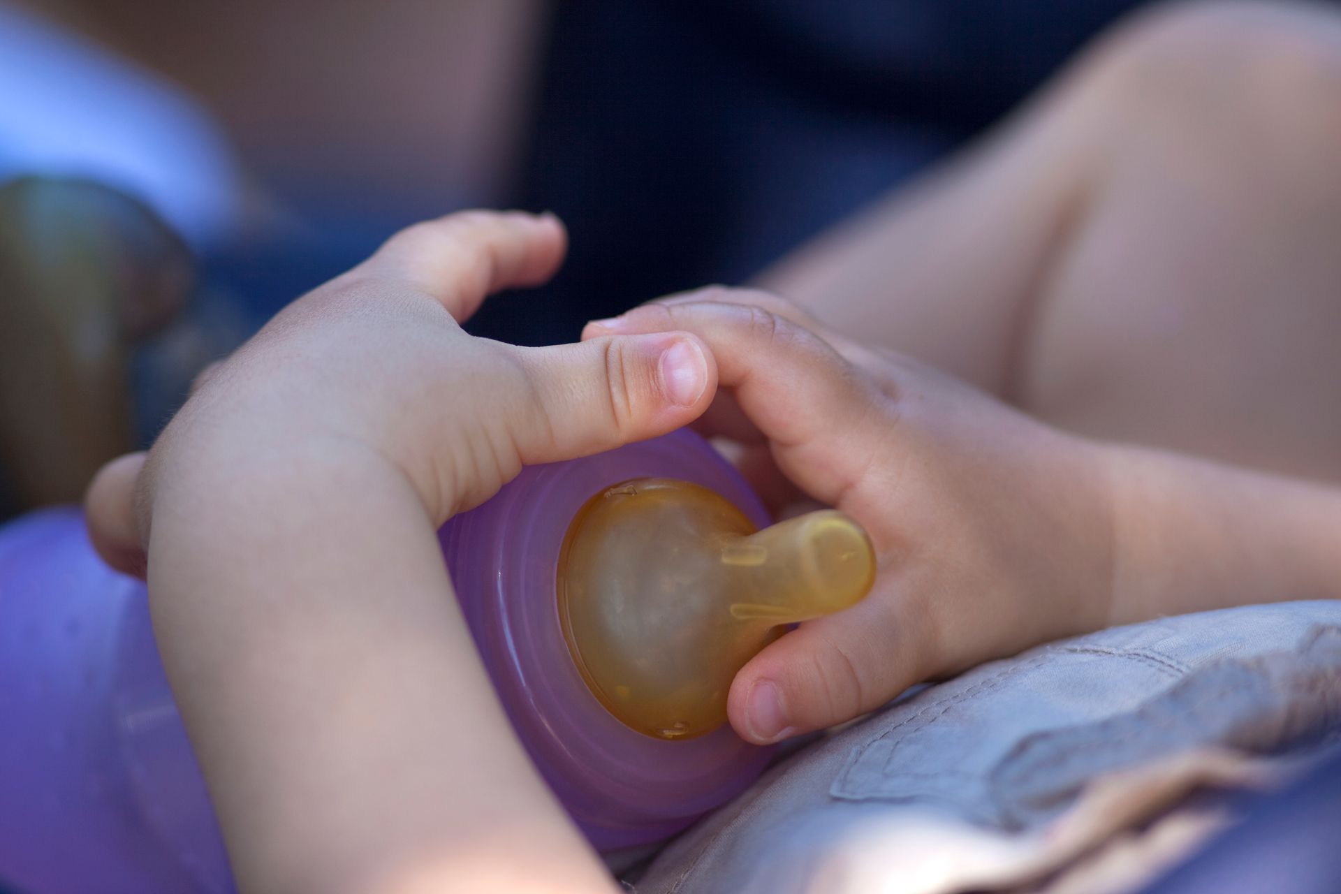 Gros plan sur des mains tenant un biberon violet à tétine jaune