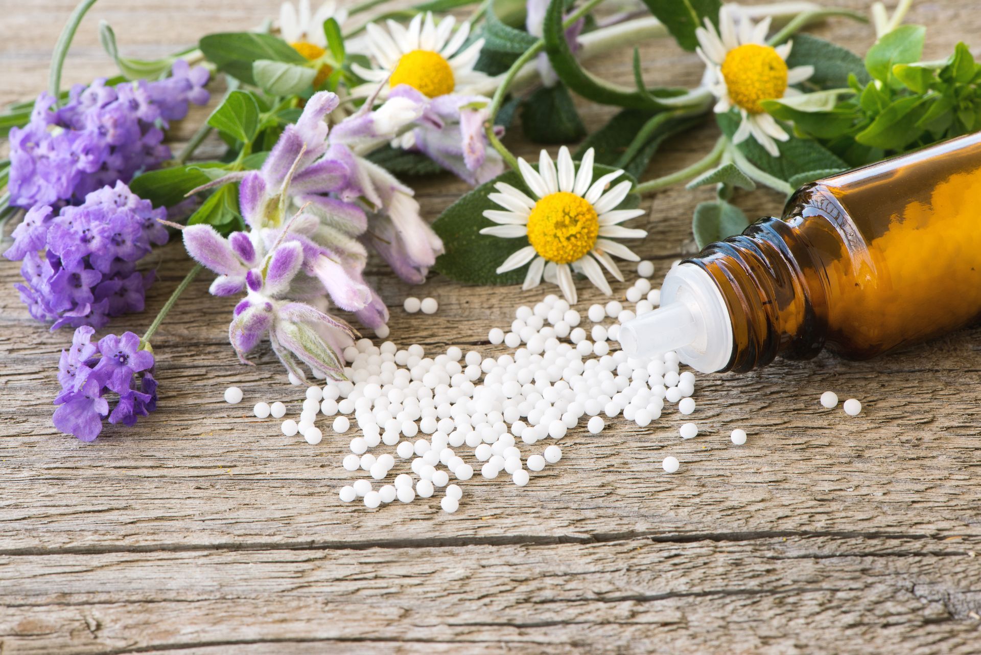 Des fleurs médicinales et des pilules blanches se sont répandues d'une bouteille ambrée sur une table en bois.