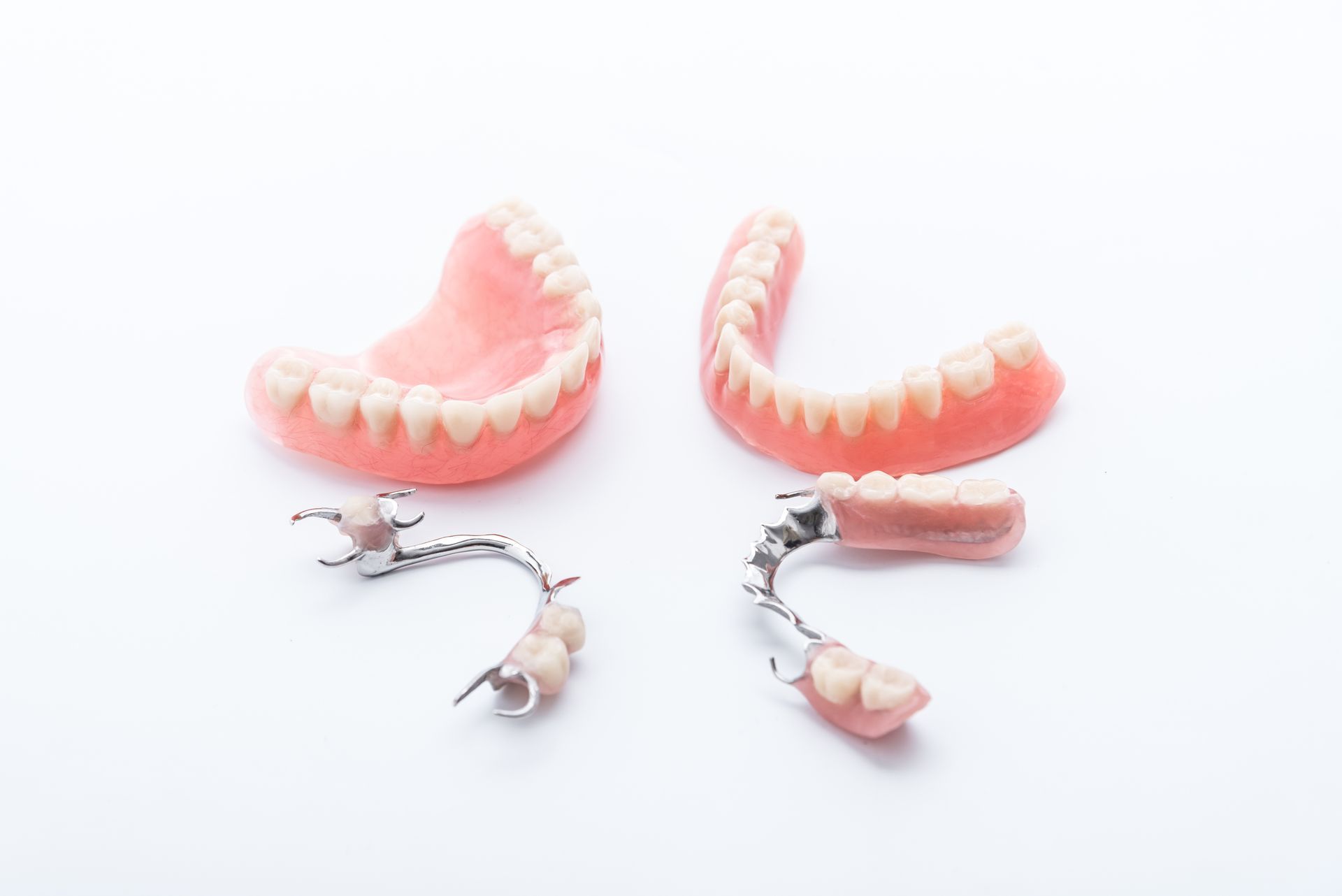 Deux dentiers roses et deux prothèses dentaires partielles sur fond blanc.