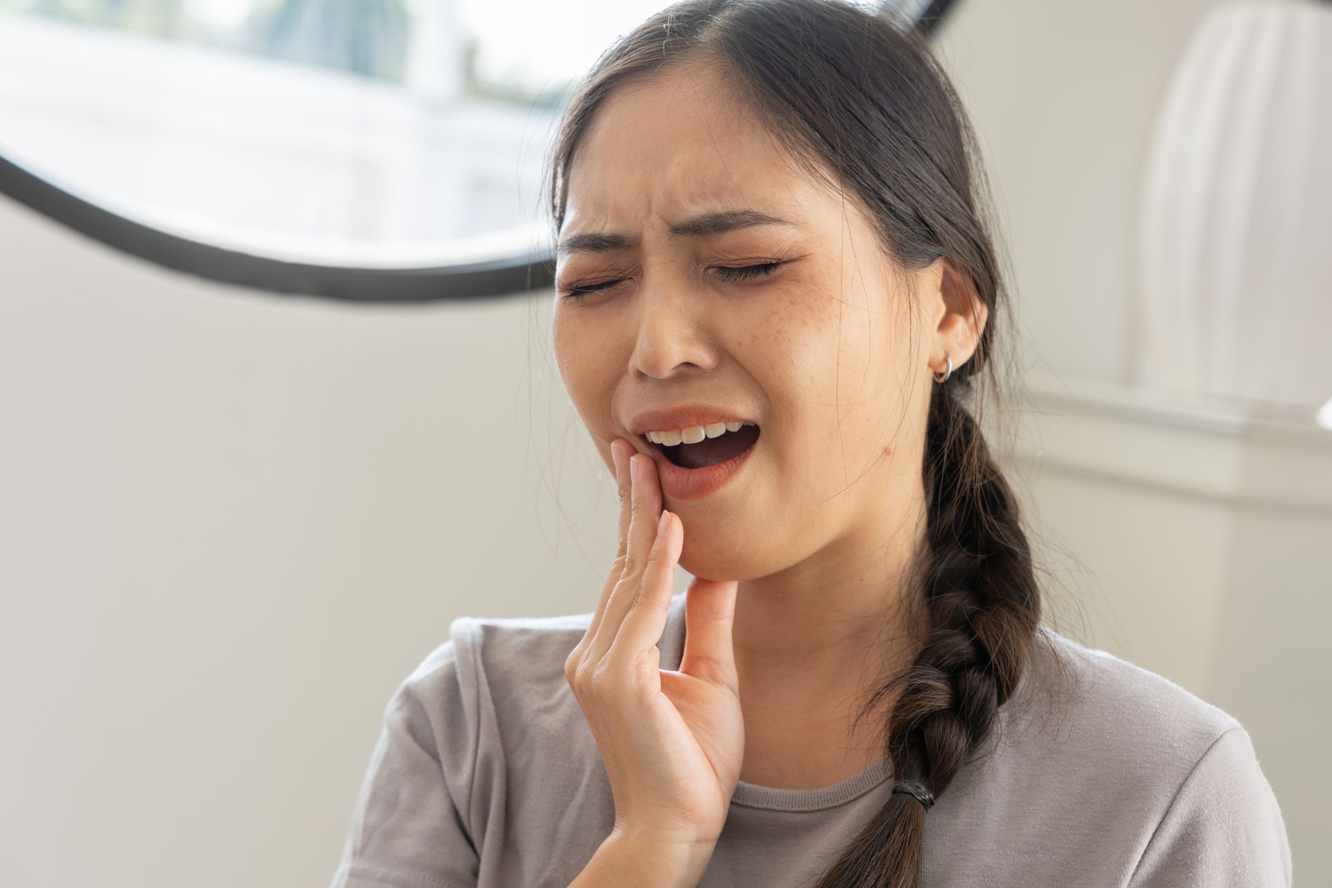 Une femme se tient la joue avec une expression douloureuse, suggérant un mal de dents.