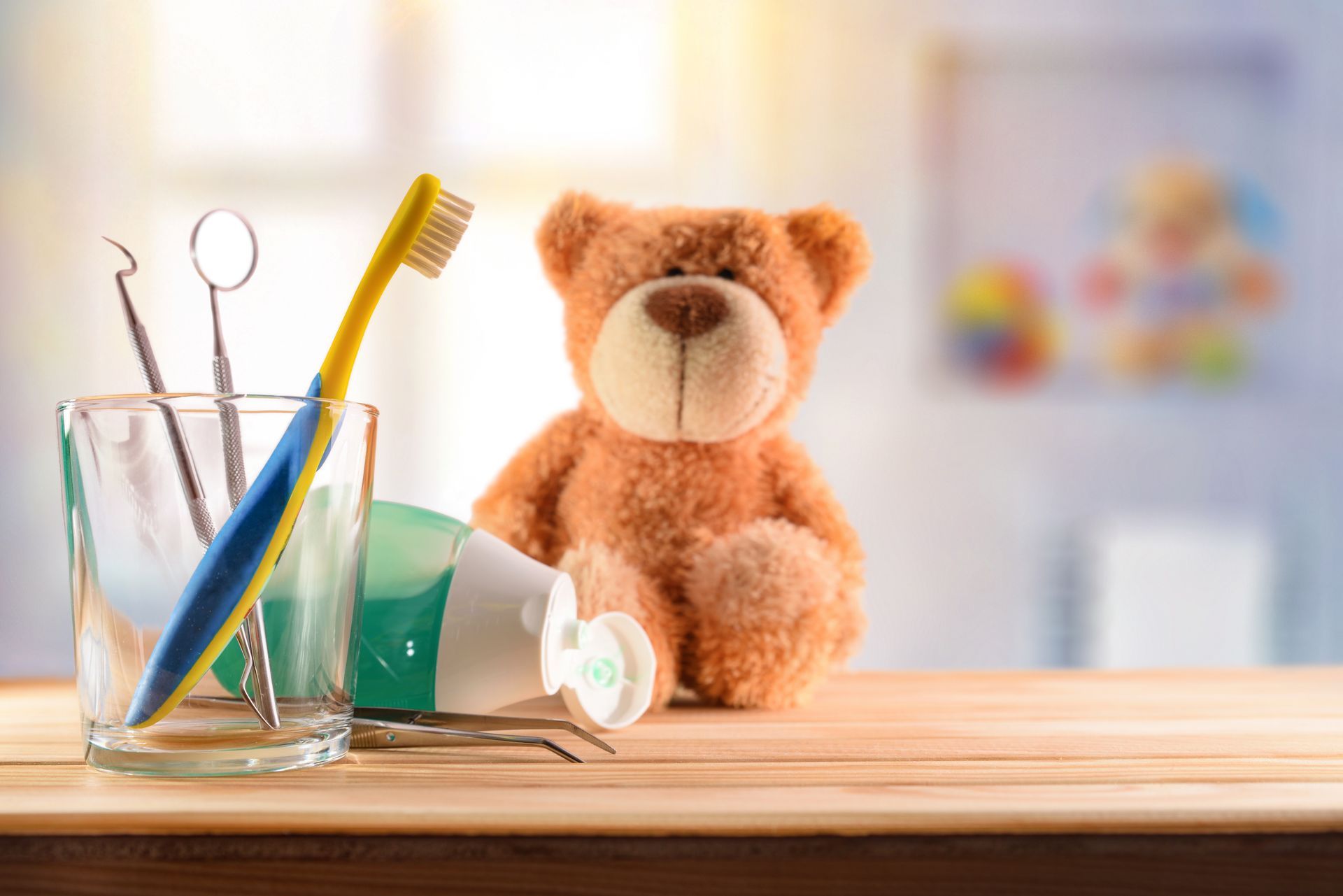 Brosses à dents pour enfants et ours en peluche sur une table en bois.