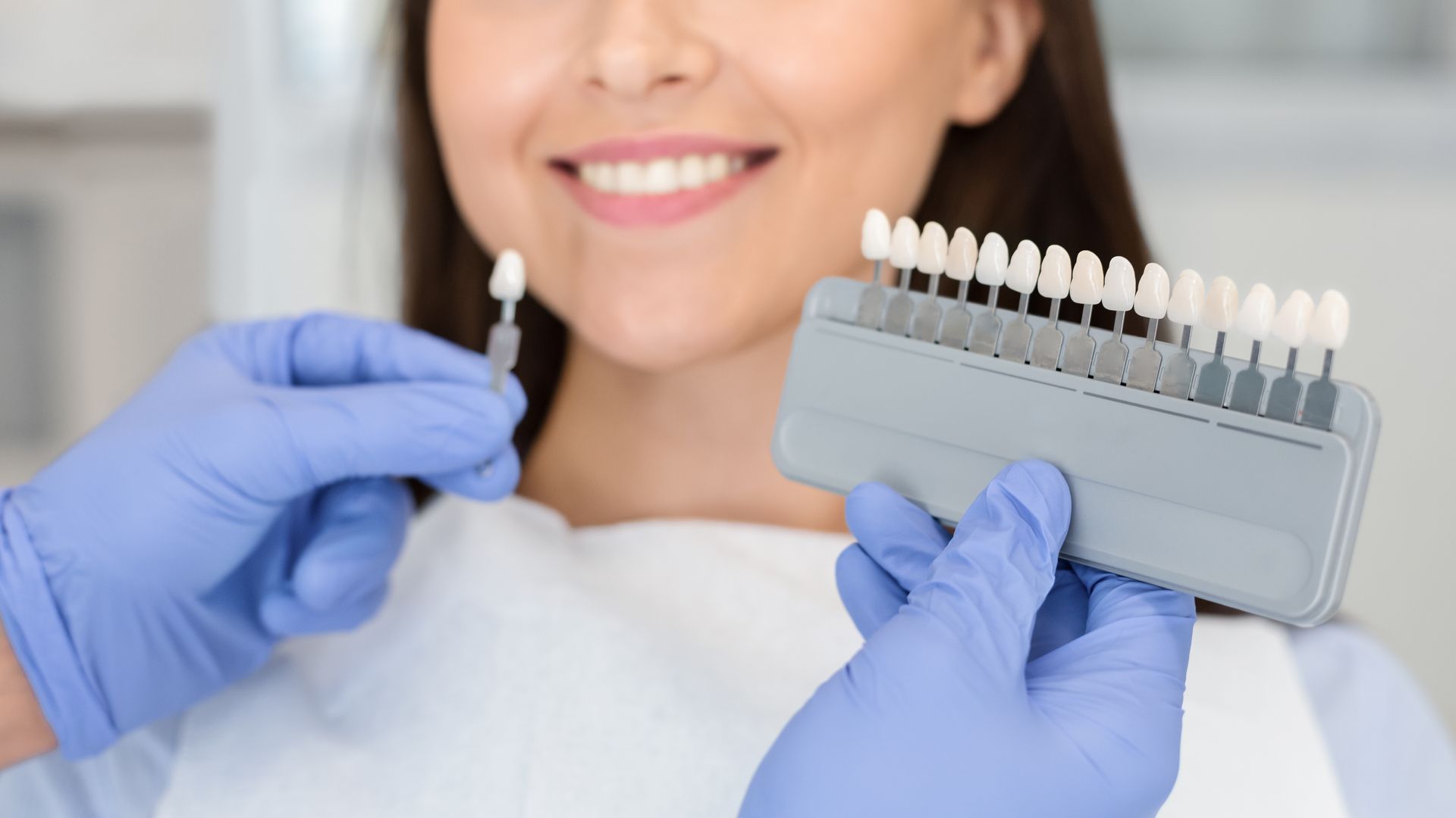 Un dentiste ganté tient un nuancier près des dents d'un patient souriant.