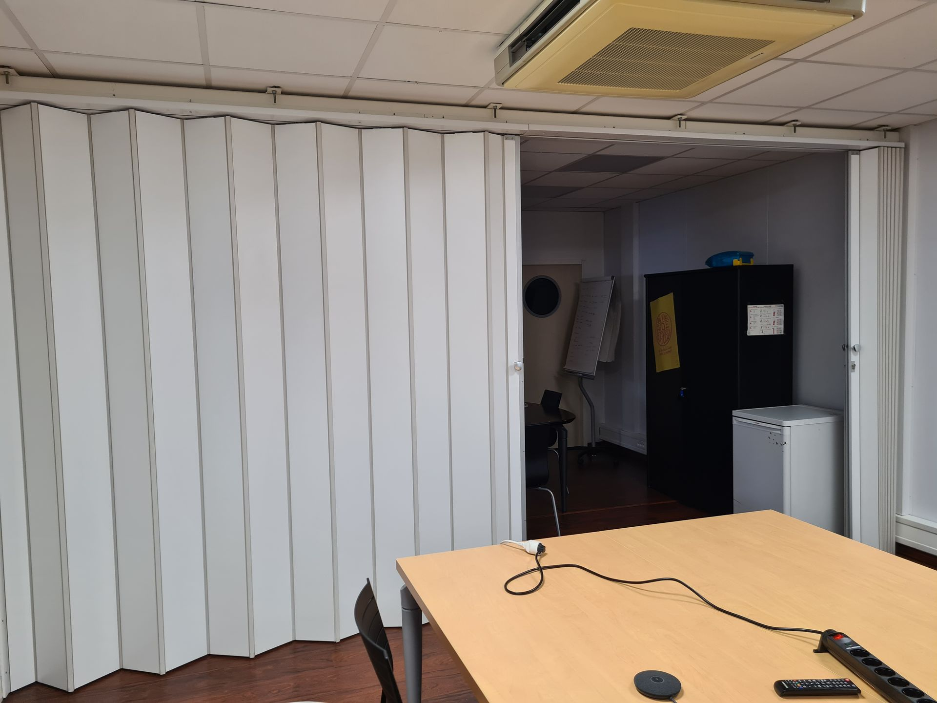 Bureau avec une cloison accordéon partiellement ouverte, une table de conférence et une armoire noire au fond.
