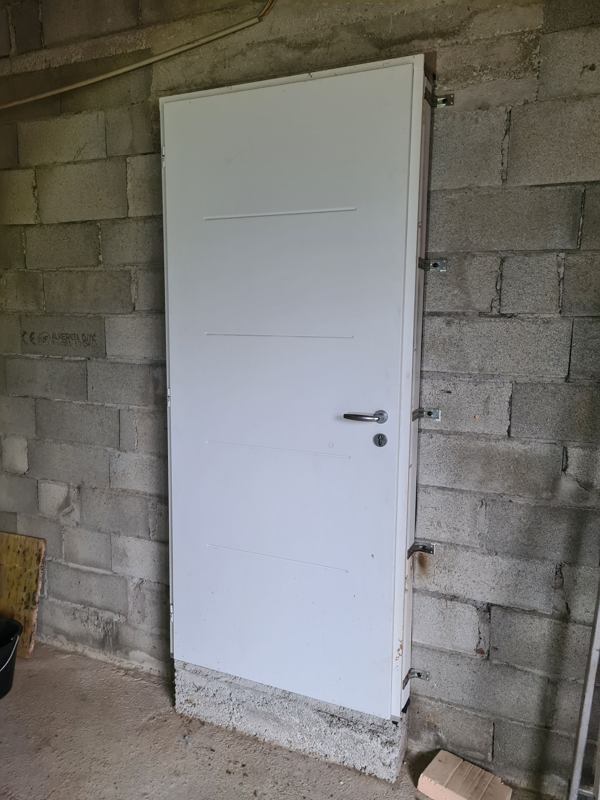 Porte blanche dans un mur en parpaings, avec une poignée argentée.