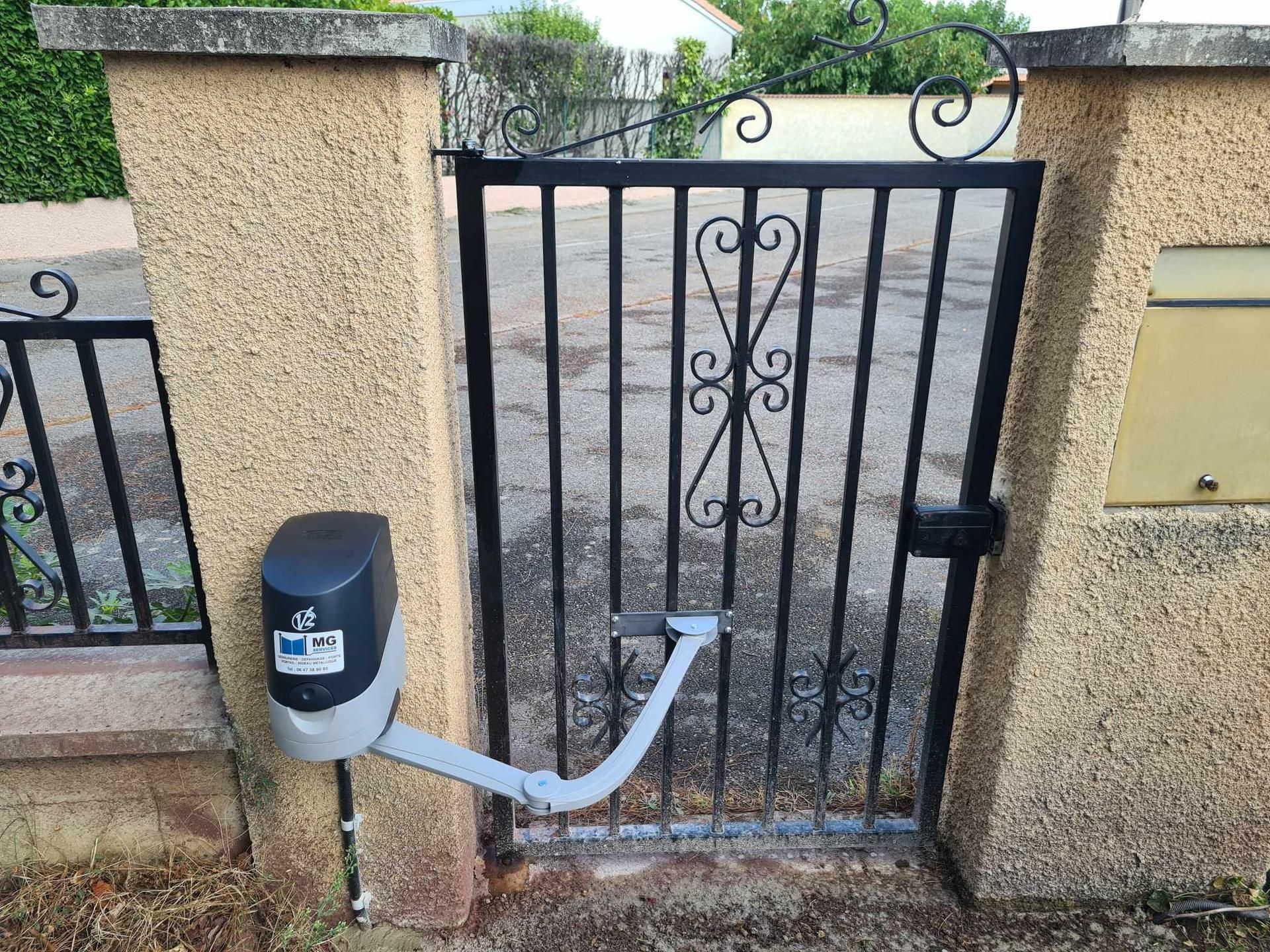 Portail de jardin en métal noir avec ouvre-porte automatique intégré entre des piliers en stuc.