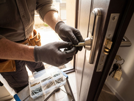 Une personne utilise un outil pour travailler sur une serrure de porte à côté d'une porte dont les clés sont suspendues à proximité.