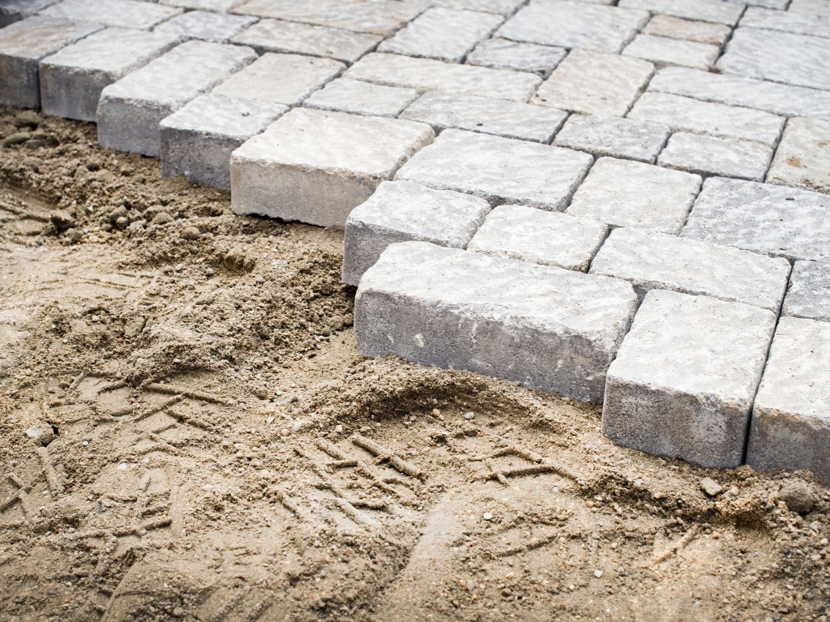 Pavés gris partiellement installés à côté d'une surface sablonneuse.