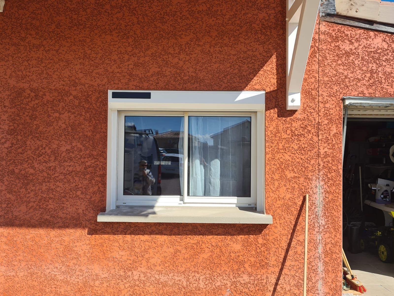 Mur d'une maison en stuc orange avec une fenêtre à cadre blanc et une porte ouverte baignée de soleil.