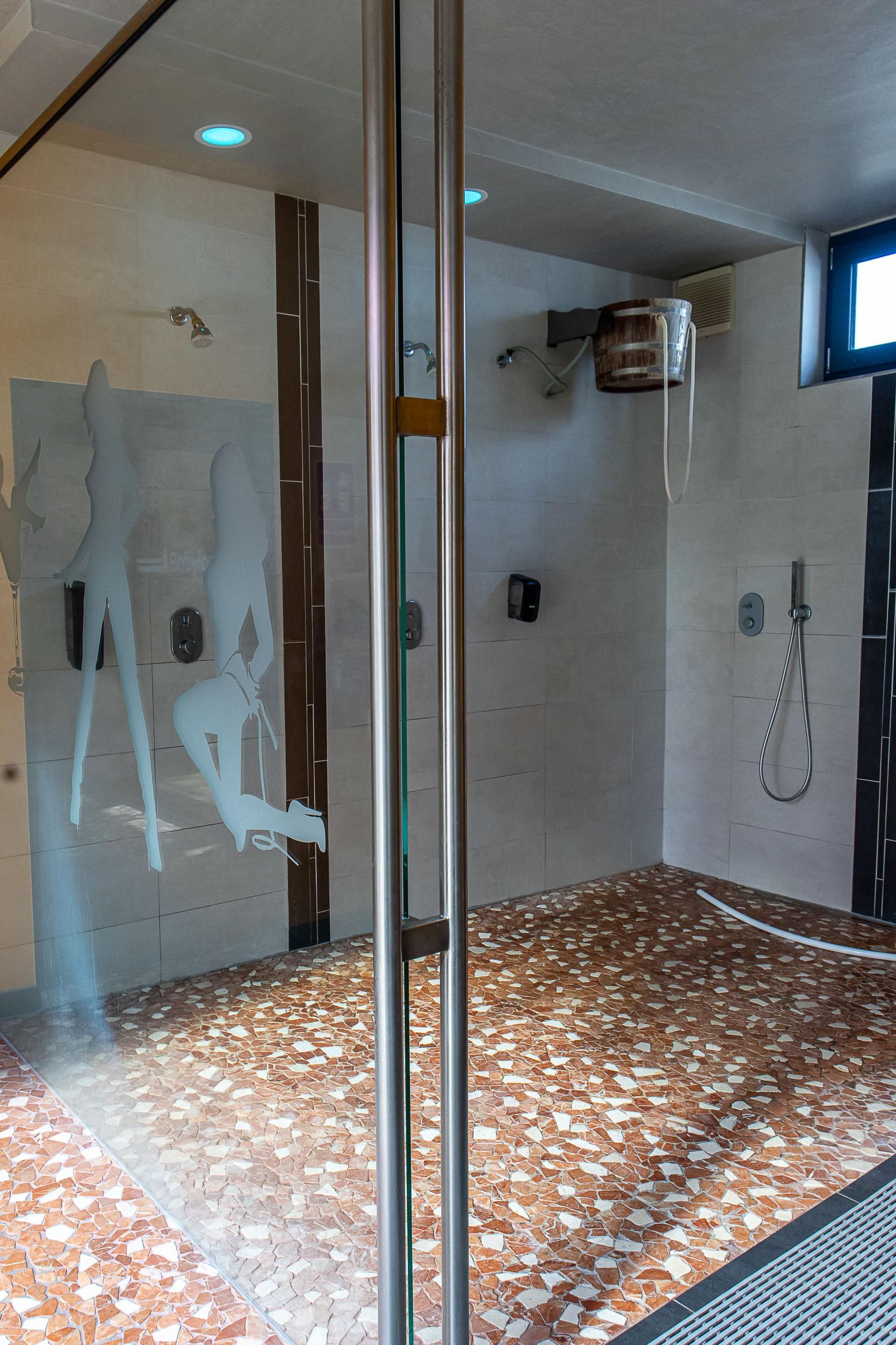 Ein Badezimmer mit Dusche und einem Eimer an der Wand.