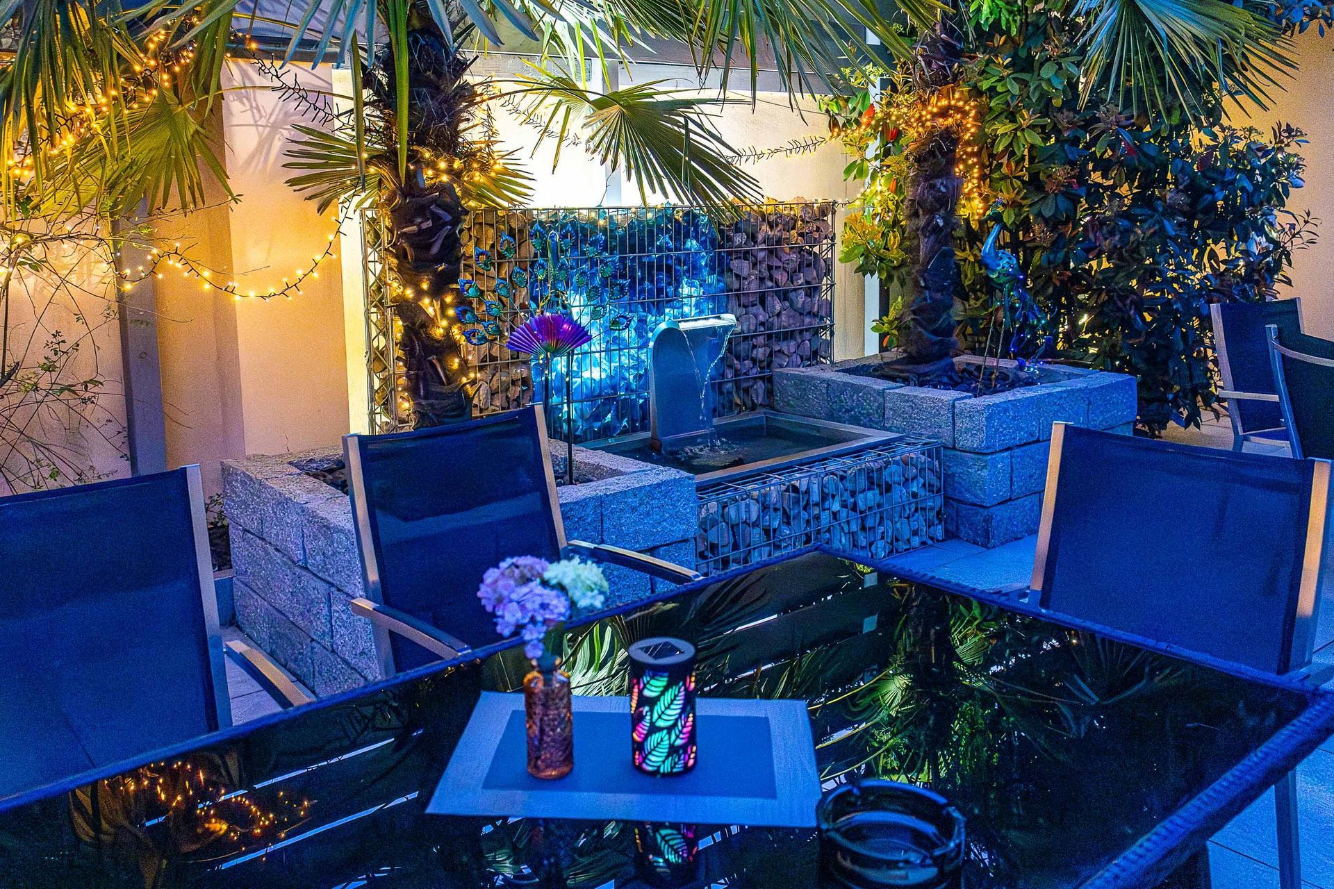 Ein Tisch mit einer Vase voller Blumen darauf in einem Garten bei Nacht.