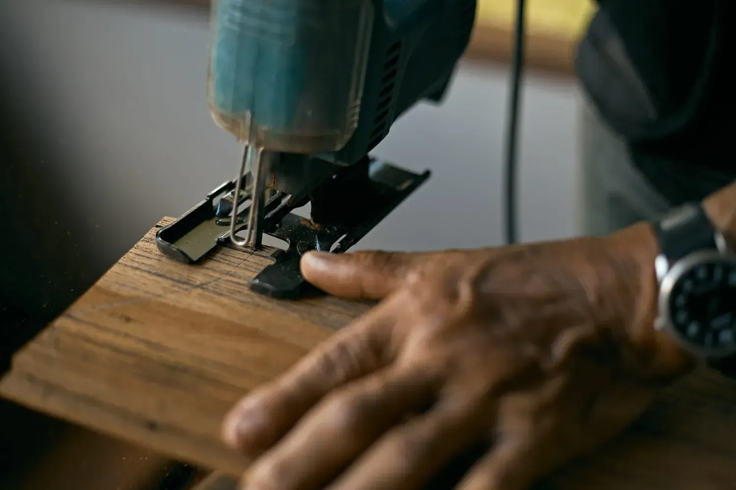 Manos guiando una sierra de calar que corta una tabla de madera sobre un banco de trabajo.