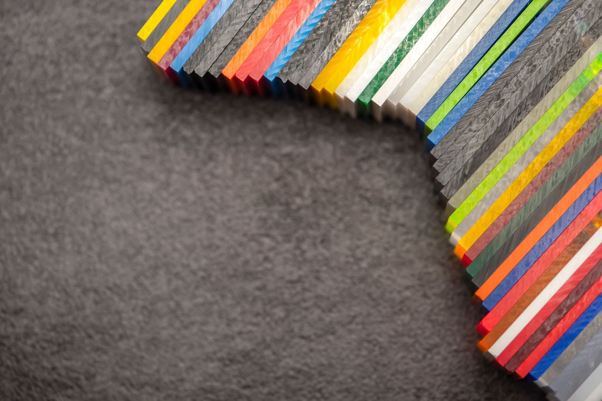 Muestras de plástico de colores dispuestas en diagonal sobre una superficie gris texturizada.