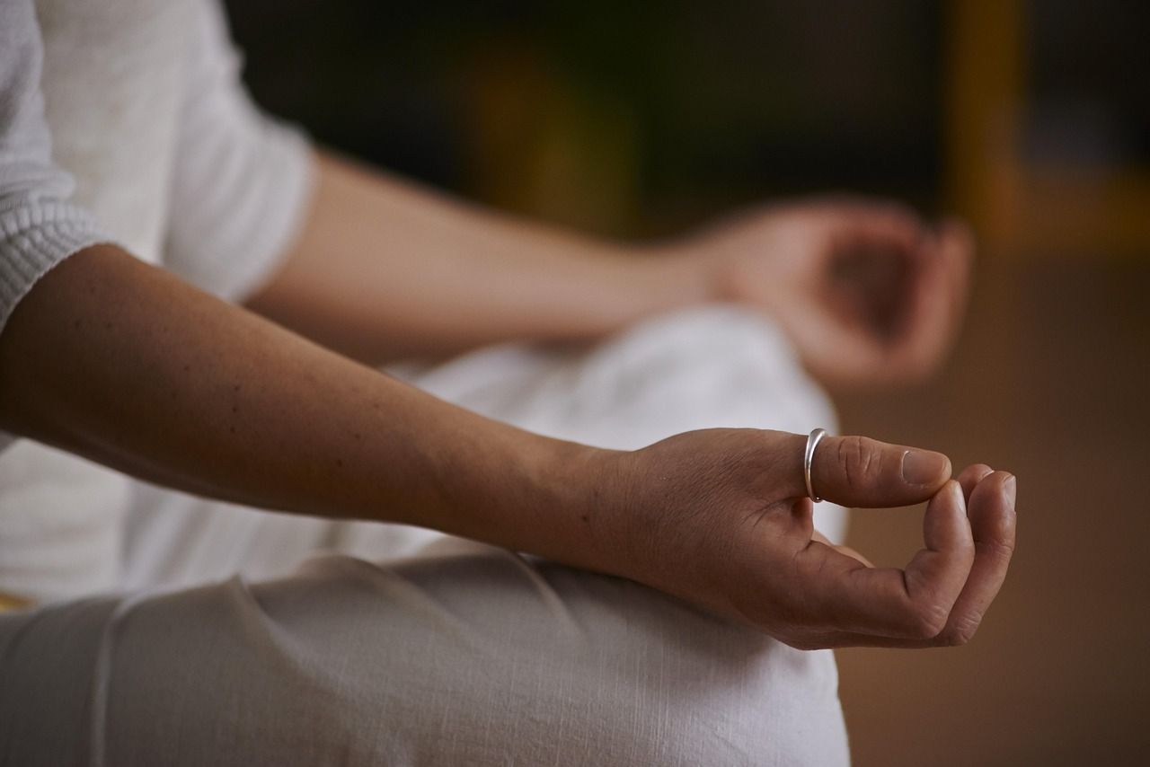 Une personne en vêtements blancs médite avec les mains en position mudra, anneau visible, à l'intérieur.