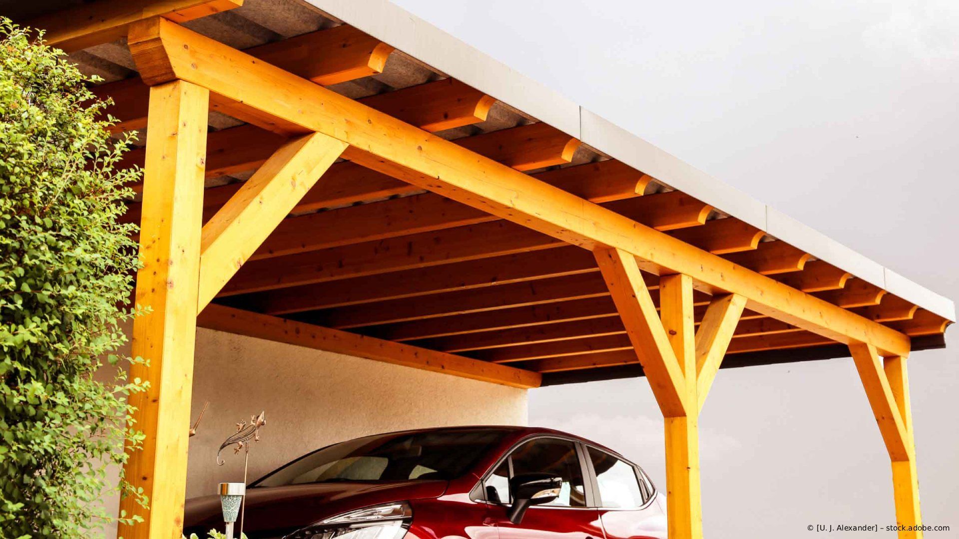 Ein hölzerner Carport mit einem darunter geparkten roten Auto neben einem Haus