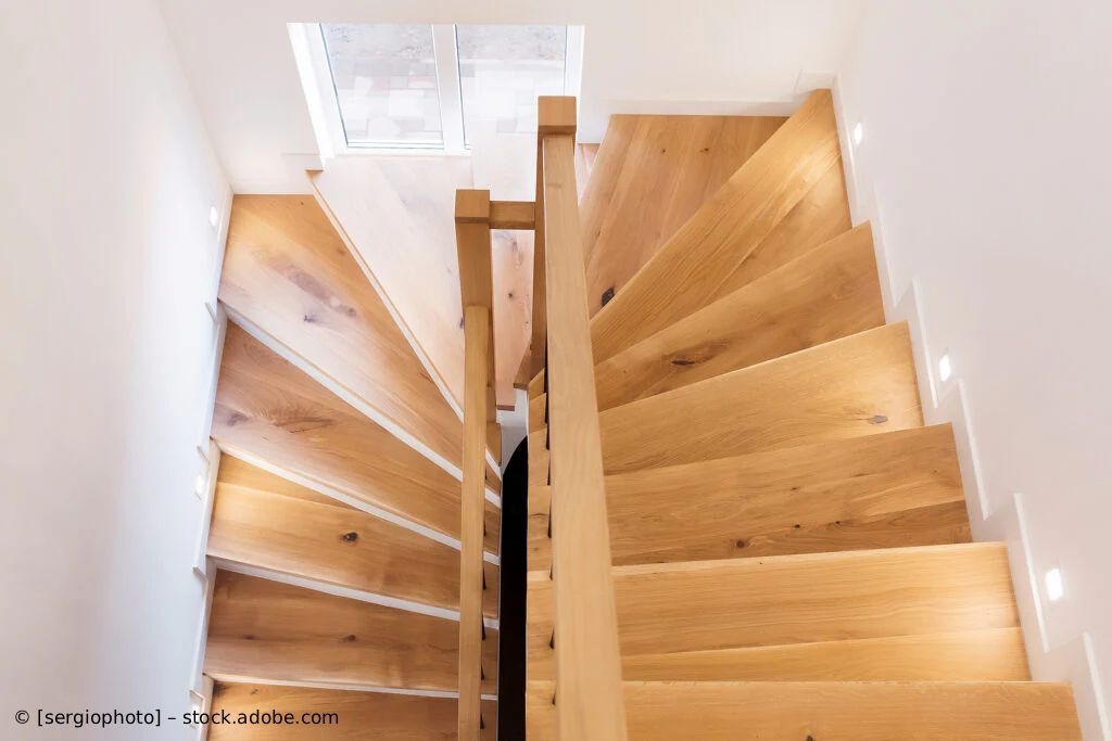 Draufsicht auf eine moderne Holztreppe mit zentralem Geländer und weißen Wänden