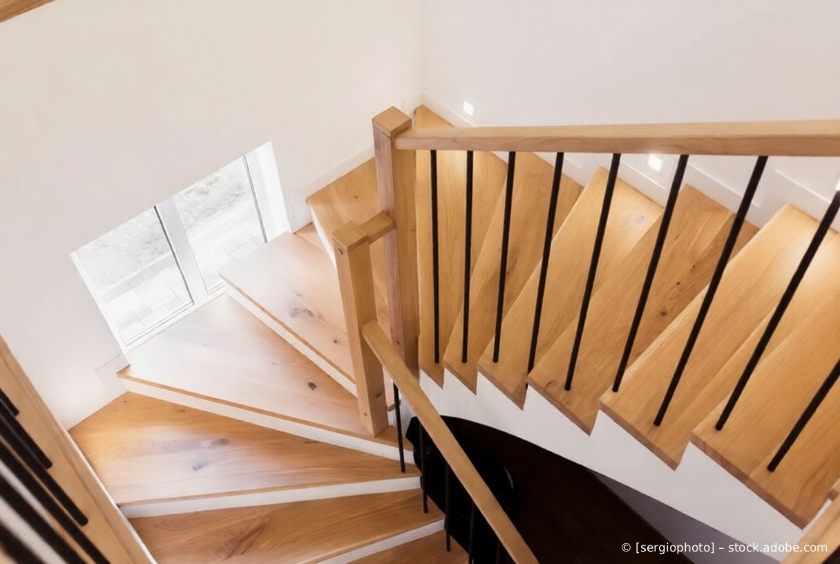 Hölzerne Wendeltreppe mit schwarzem Geländer neben einer weißen Wand und Jalousien