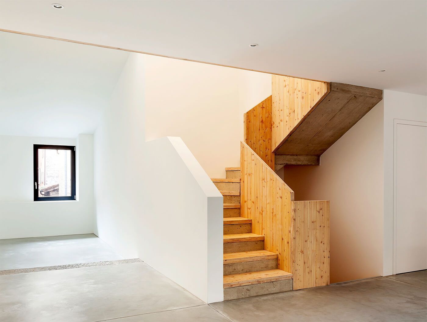 Modernes Interieur mit weißen Wänden, kleinem Fenster und unfertiger Holztreppe mit Treppenabsatz.