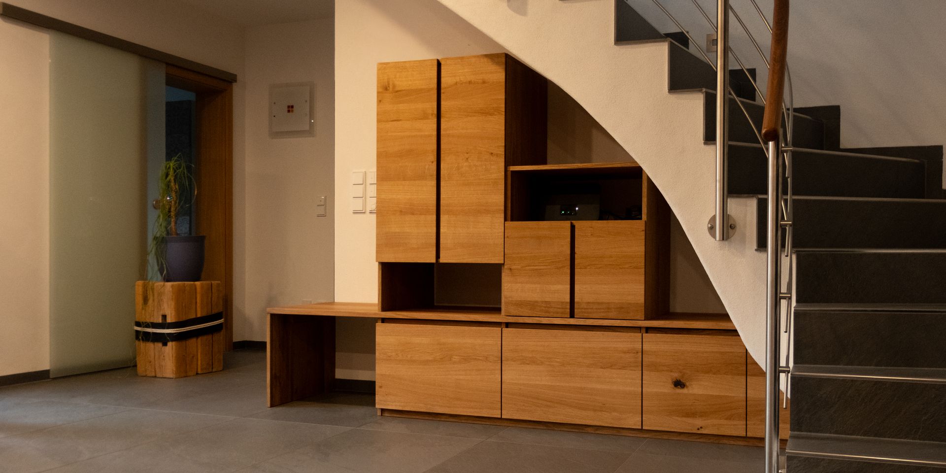Eingebautes Holzregal mit verschiedenen Fächern und einer Glasvitrine, beleuchtet von einer Pendelleuchte.