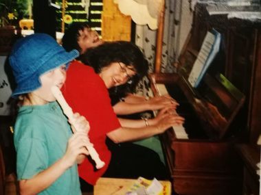 Ein Kind spielt Blockflöte; zwei Erwachsene spielen drinnen zusammen Klavier.