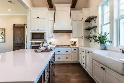 Una cocina con gabinetes blancos, una estufa, un fregadero y una isla grande.