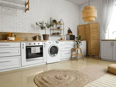 Una cocina con muebles blancos, una lavadora, un horno y una alfombra.