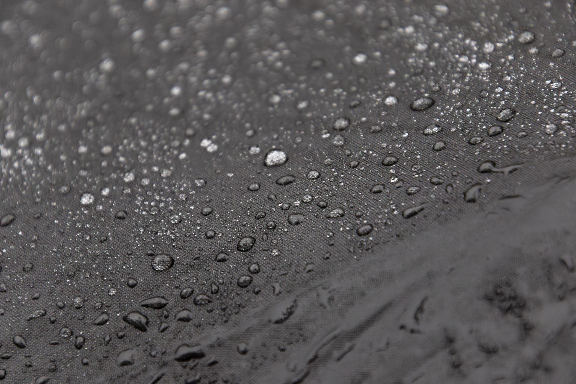 Gros plan sur des gouttelettes d'eau transparentes perlant sur une surface sombre, texturée et résistante à l'humidité.