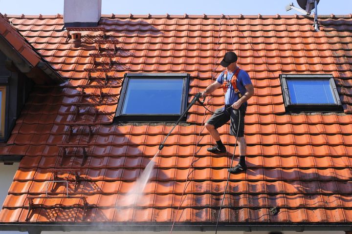Deux ouvriers, en plein air et sous un soleil radieux, utilisent des marteaux pour installer des supports en bois sur un toit recouvert d'une sous-couche noire.
