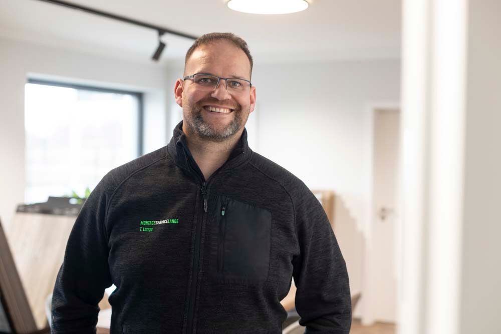 Ein Mann mit Brille und schwarzer Jacke lächelt in die Kamera.