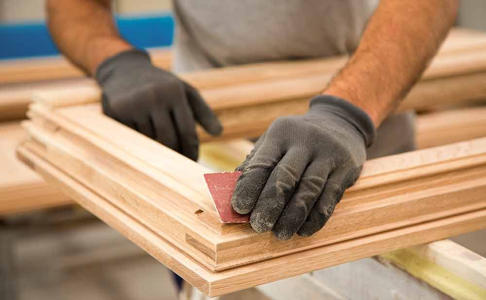 Ein Mann mit Handschuhen schleift ein Stück Holz.