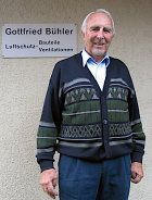 Ein Mann im Pullover steht vor einem Schild.