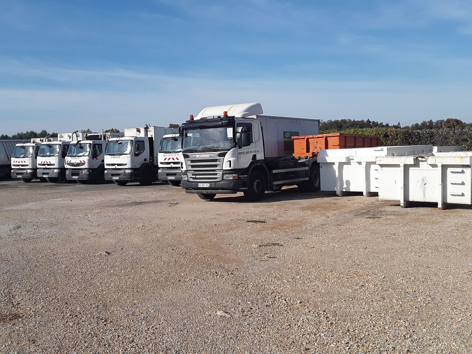 Camions et bennes à ordures dans une cour de gravier.