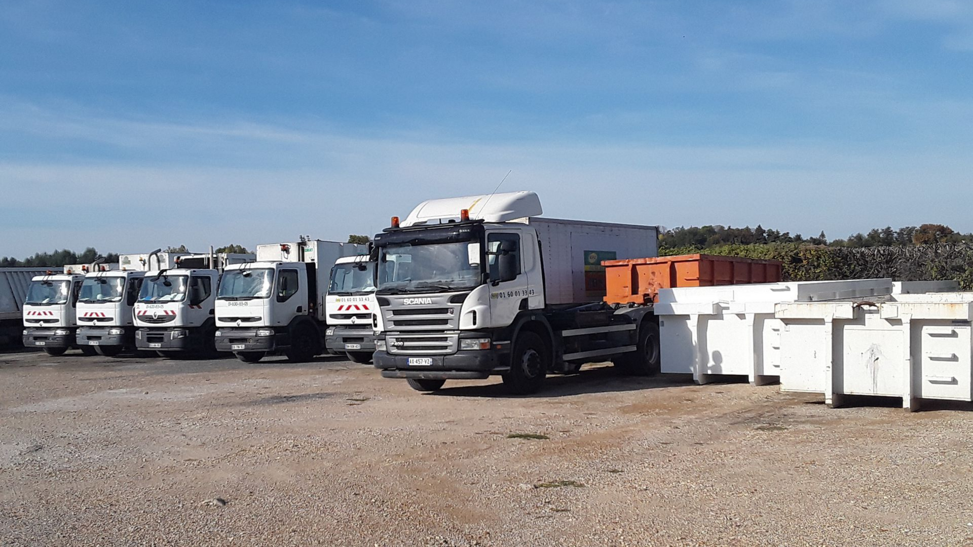 Camions et conteneurs à déchets sur un terrain extérieur.