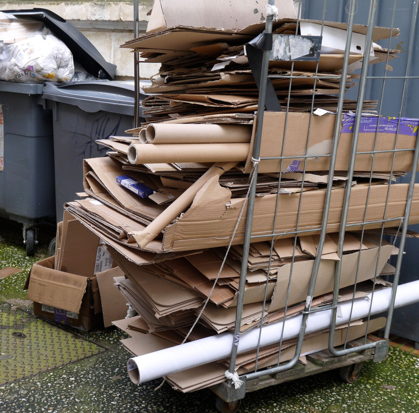 Chariot débordant de cartons et de rouleaux de papier, à côté d'une poubelle.